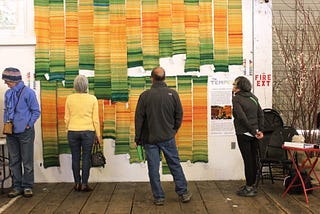 A collection of knitted Tempestries hanging vertically on the wall of a gallery.