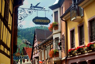 Colorful facades in an alley in Kaysersberg with an old sign showing the name of the town.