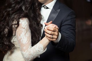 A cropped image of a bride and groom dancing, highlighting their closeness and hands clasped.
