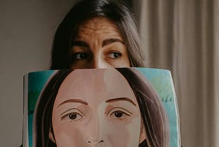 A woman holding a drawing of herself as a mask.