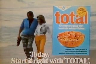 A freeze frame from a late 1970’s television advertisement for Total cereal; a couple walk arm in arm along a beach, paired with an overlay showing a box front of Total and the text: “Today. Start it right with ‘TOTAL.’”