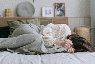 Women lying on a bed, crying into a blanket