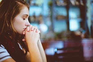 A frustrated woman sitting with her eyes closed and clasped hands resting on her chin.