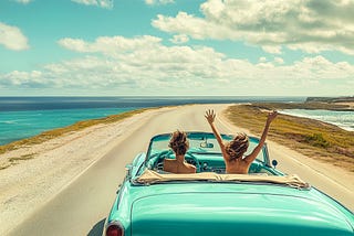 Two women driving along hte coast in a turquoise convertible, feeling the wind in their hair