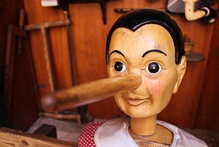 Picture of a wooden doll, similar to Pinocchio, with a long nose, signifying deceit.