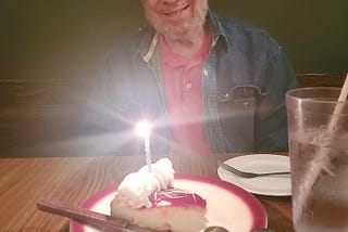 man sitting with cake + candle at restaurant table