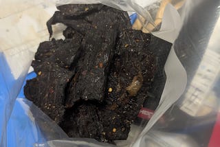A plastic zip-top bag of homemade whole-muscle jerky, as seen looking down into the open top of the bag.