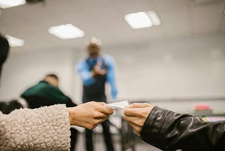 Two students passing notes in a classroom who are caught by a teacher.