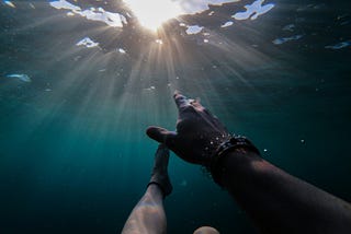 A drowning man reaches for the blue sky visible above the water