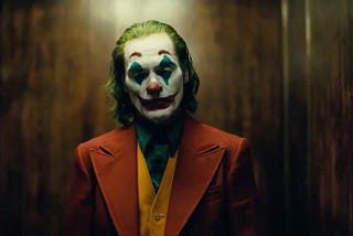 Joaquin Phoenix, as the Joker, with crisp clown makeup on, including blue triangles above and below his eyes, and a red smile