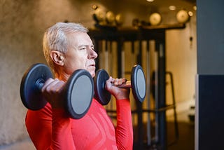 Older man doing resistance exercises with heavy dumbbells.