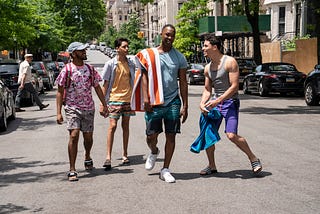 A scene from In The Heights featuring several characters standing on a road.