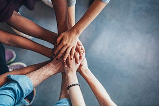 Overhead image of five pairs of hands piled on top of one another to signify teamwork.