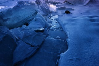 Snow banks next to a narrow river at dawn — a winter’s dawn with the rising sun a beacon on the whole scene