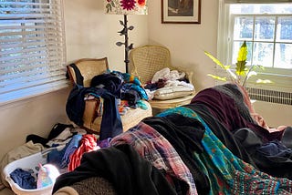 Room with clothes on bed, chairs and in a laundry basket.