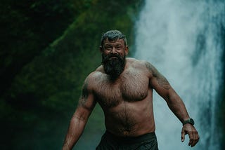 Candid photo of a tattooed bearded man in water next to a waterfall