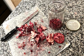 Messy deconstructed pomegranate and seeds with a knife on a kitchen counter
