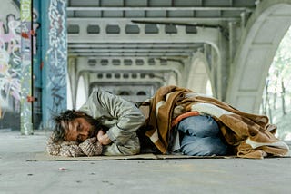 A homeless man lying outdoor under an overpass.