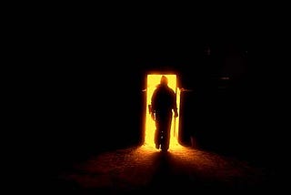 Person walking from darkness into doorway full of light