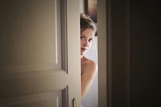A woman peeking out from behind a partially open door.