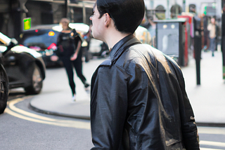 AI image of a pale man with black hair wearing a leather jacket and walking through London.