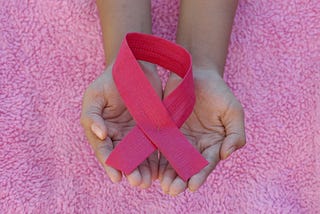Hands holding a pink ribbon.