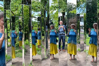 Selfie of the author reflected in multiple mirror panels with a man, unreflected also taking a selfie. Setting is outdoors among summer trees, colors are blues and yellow-greens.