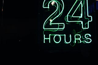 Placa em neon, com as palavras “Aberto 24 horas” brilhando em um azul claro