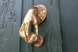 A golden door knocker in the shape of a hand delicately holding an apple.