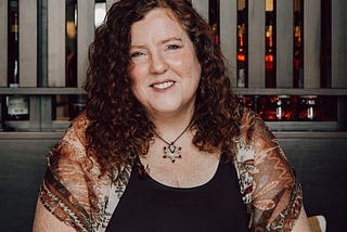 Photo of Della in brown print outfit at coffee shop table