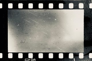 Burned black and white film strip with faint distortions and scratches against a white background.