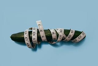Photograph of a cucumber with a tape measure wrapped around it.
