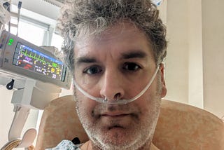 Author in intensive care with tubes inserted and monitors visible.