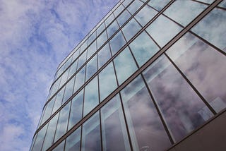 A glass and steel skyscraper shot from below, against a partly cloudy sky.