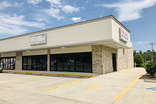 An image of a concrete building in front of a parking lot. The signs are faded and there is a signboard that says, “For Lease.”