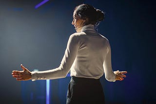 Female public speaking on stage with open arms