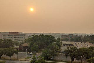 A photo captures the wildfire haze covering an area of Greenbelt, Maryland, with buildings in the forefront. The background of the image is difficult to make out due to the haze.
