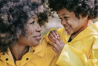 Photo of a woman and a child wearing yellow raincoats. Symbolizes a mother and daugher, raincoats symbolise self care to stop yourself from drowning.