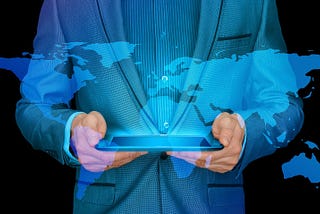 Man in a suit holding a digital tablet device, with a blue overlay of the contintents of the globe.