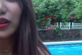 An Asian woman taking a selfie in daylight. In the background is an  apparation of a ghost staring over her shoulder.