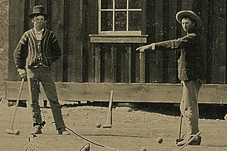 Photo de Billy the Kid et un membre inconnu des régulateurs en train de jouer devant une maison en bois.