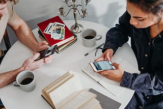 A young couple sitting across from each other both using their phones for entertainment.