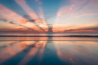 A photo of the ocean, the horizon-line evenly splits the frame. A cloud is poised above the horizon, bright pink sun rays.