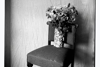 Black & White photograph of a bouquet of flowers standing on a chair.