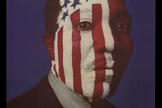 Black man’s face with red & white stripes/blue stars painted on it; excerpts from the Pledge of Allegiance at top of poster.