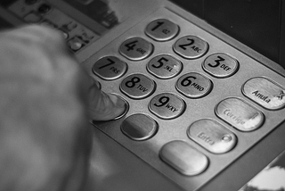 A black and white picture of someone pressing the buttons on an ATM.