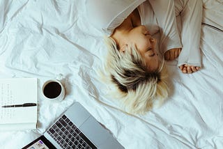 woman sleeping on a bed with laptop and open notebook nearby