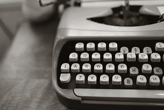 An antique typewriter with a sheet of paper sitting on a wooden desk. Photo by Leah Kelley: https://www.pexels.com/photo/close-up-photo-of-gray-typewriter-952594/