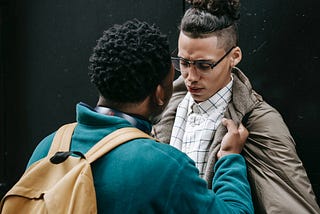 Two young men fighting. One slamming the other against a wall by his jacket.