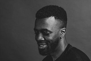 A black and white headshot of Daniel, a Black man with a fade who is smiling slightly in a black t-shirt